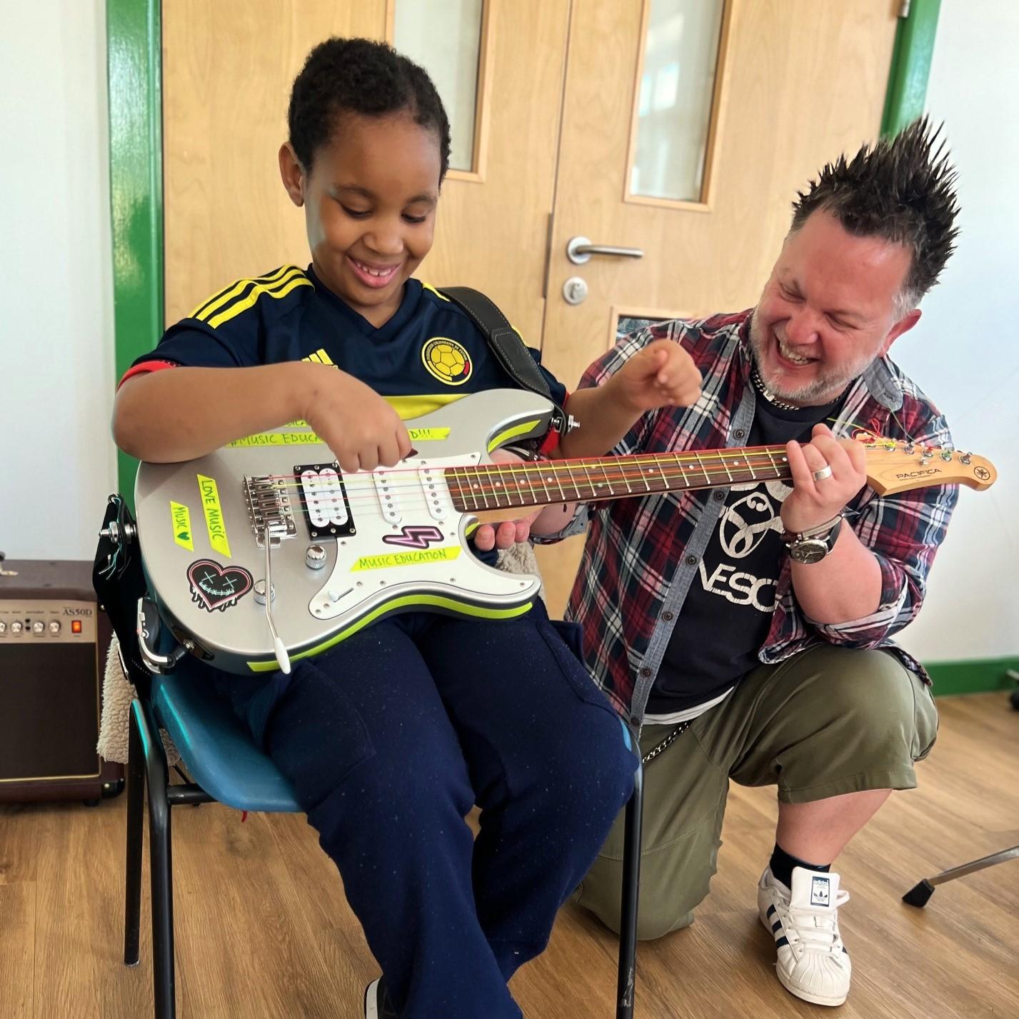 Young person playing the guitar with a music therapist