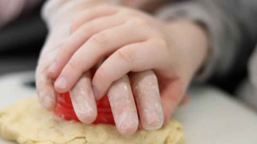 Child's hand on top of carer's hand whilst pressing a shape cutter into dough