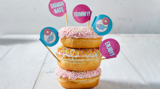A stack of three doughnuts with signs saying National Doughnut Week, Dough-nate, yummy, and Enjoy.