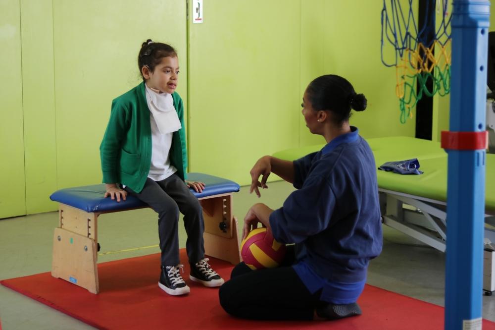 Shakeerah sitting with her physiotherapist, she is signing 'walking' to her