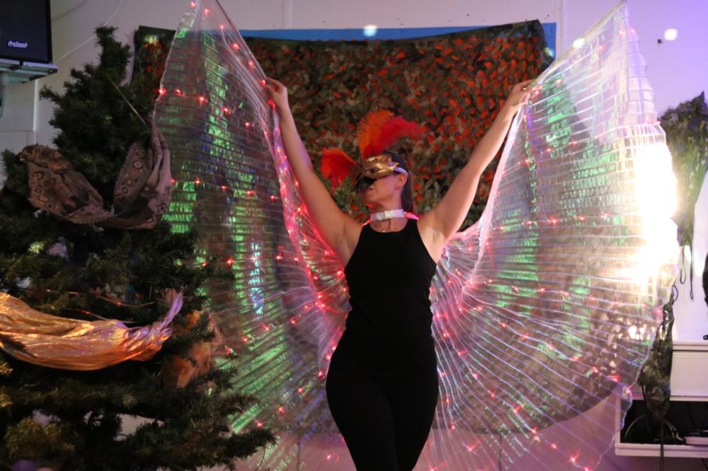 A dancer in a costume of mask, feathers and large lit-up wings