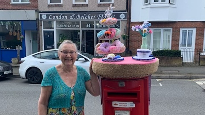 local supporter stood next to post box with her knitted doughnut post box topper in place.
