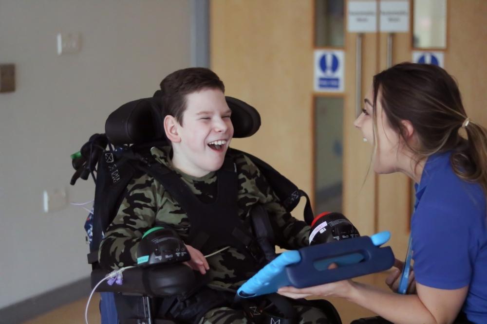 William laughing with his speech and language therapist. She is holding up an ipad.