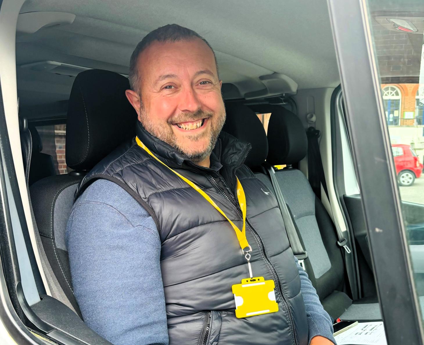 Graham sits in a van, smiling. He is wearing a yellow lanyard.