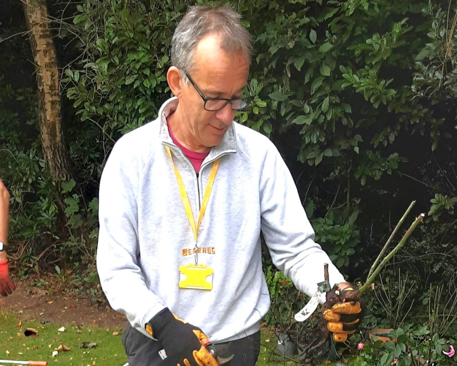 Nick is outside wearing gloves and holding gardening tools