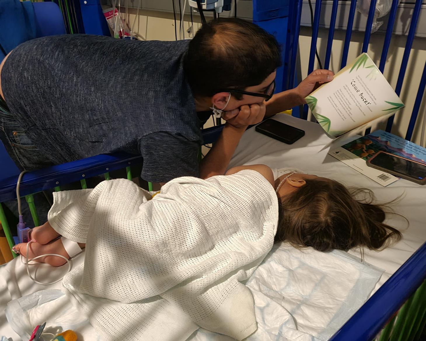 Orion lying in a hospital being read a book