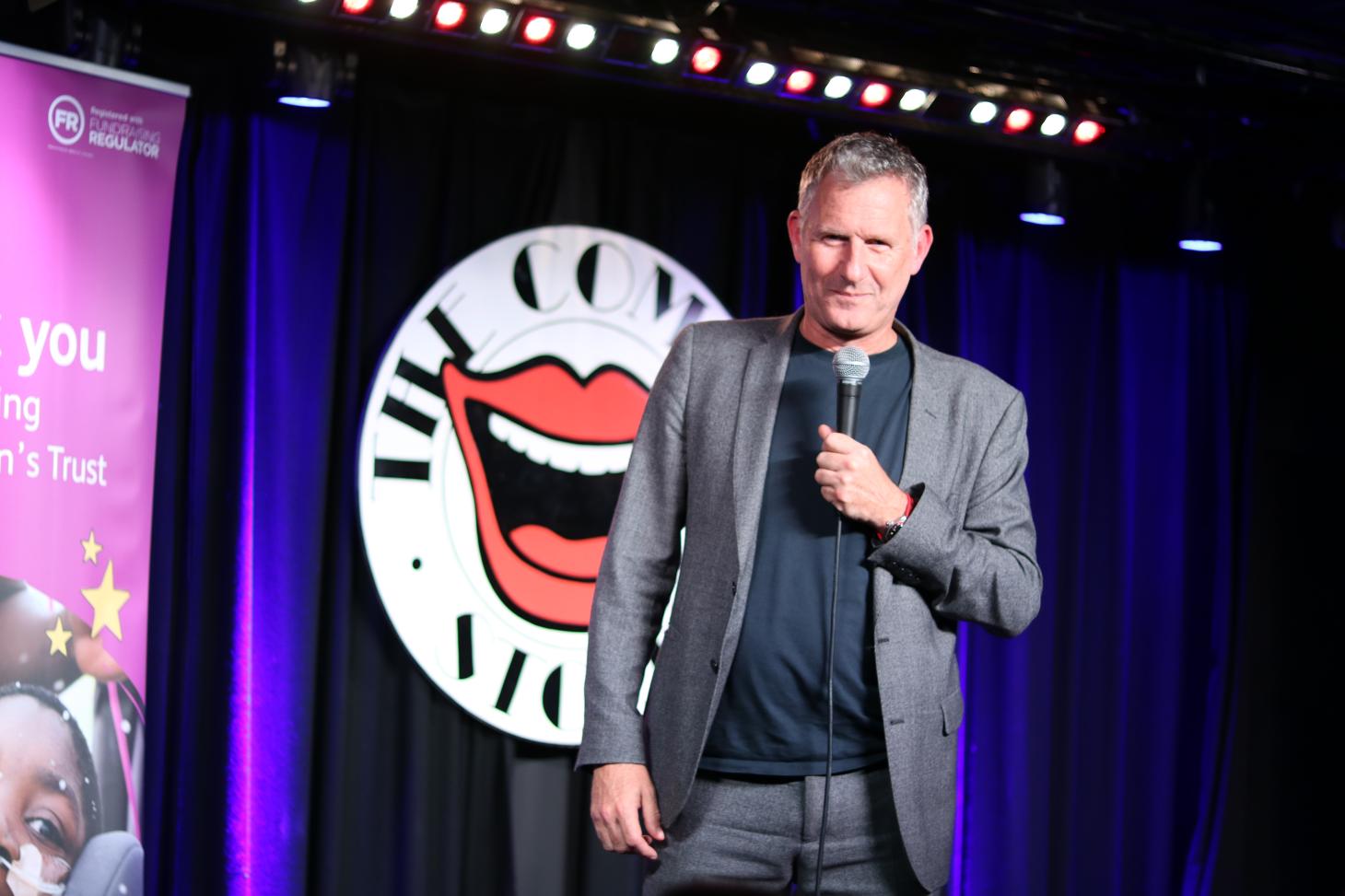 Adam Hills holding a microphone