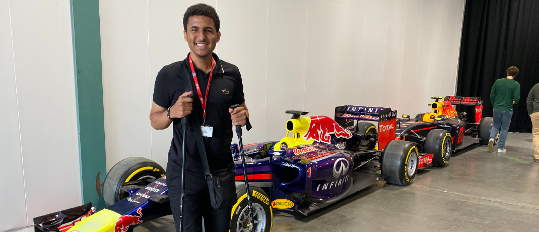 Zac standing and smiling in front of a series of race cars.