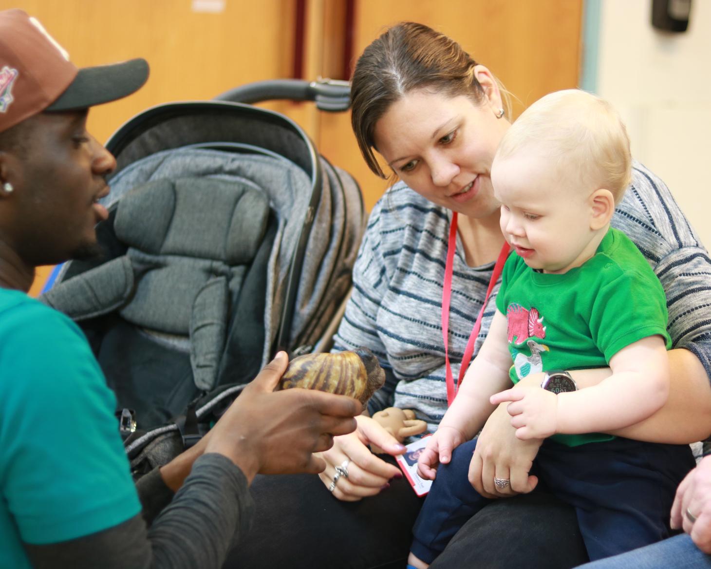 Isaac sitting on his mums lap, looking at a tortoise being held up in front of him