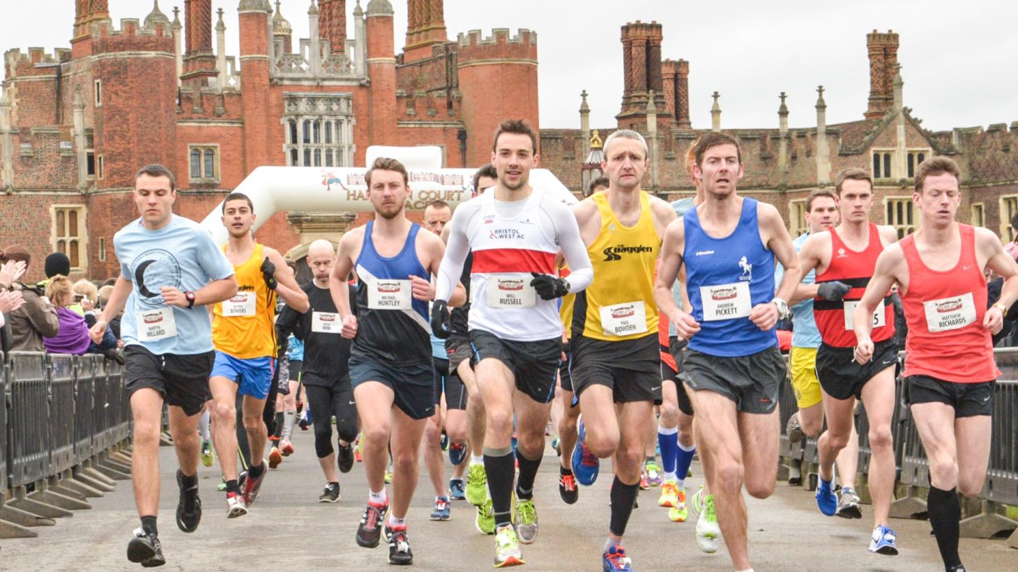 runners running toward camera on path in front of red brick Hampton Court Palace