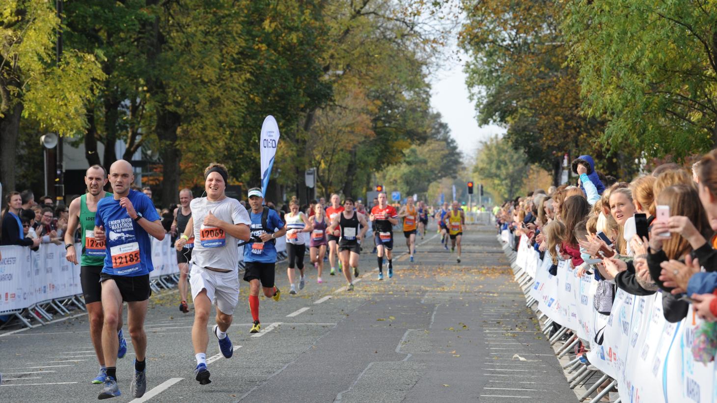 runners on road amongst trees and white banners lining the street of supporters