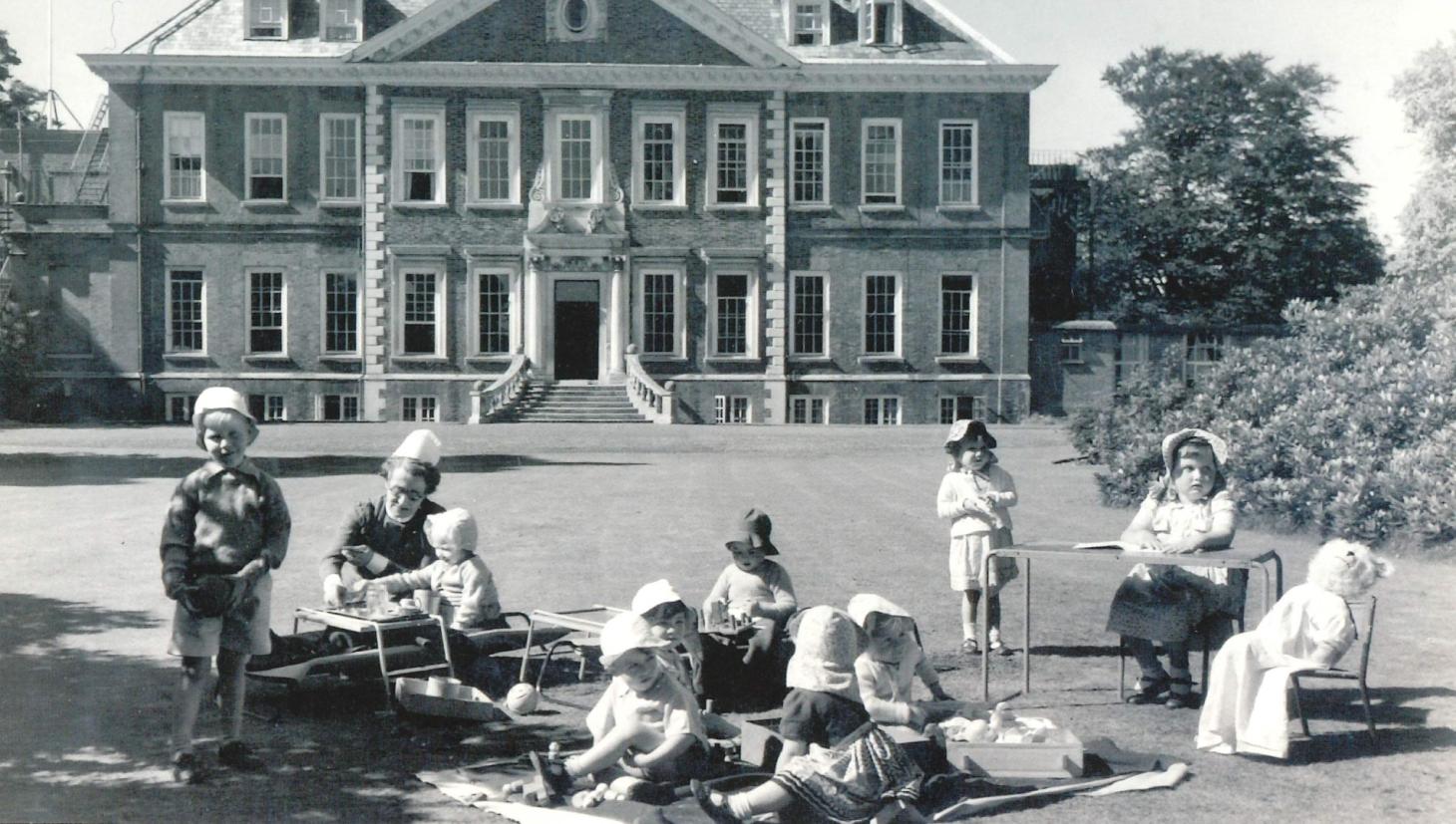 children sitting in the gardens in front of the mansion.