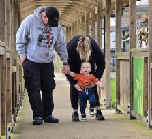 Isaac walking with help from therapist and holding dad's hand