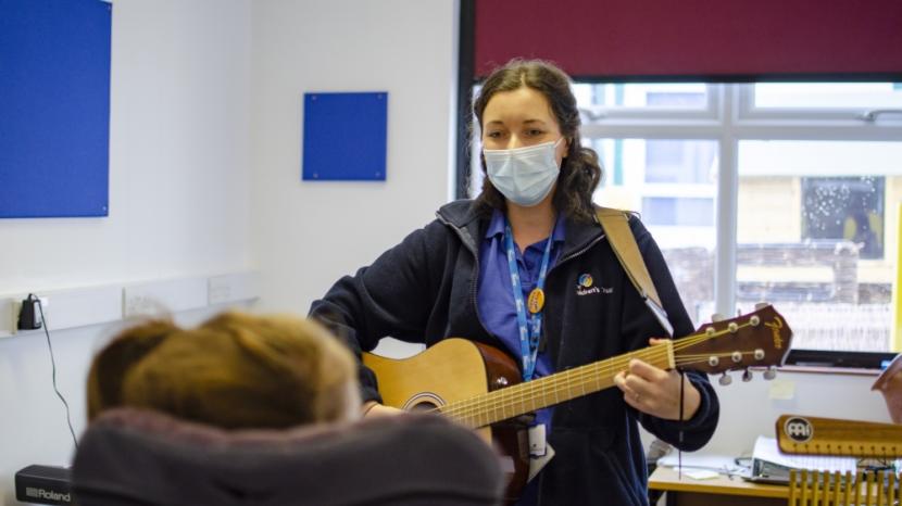 Music therapist playing a guitar in front of a young person