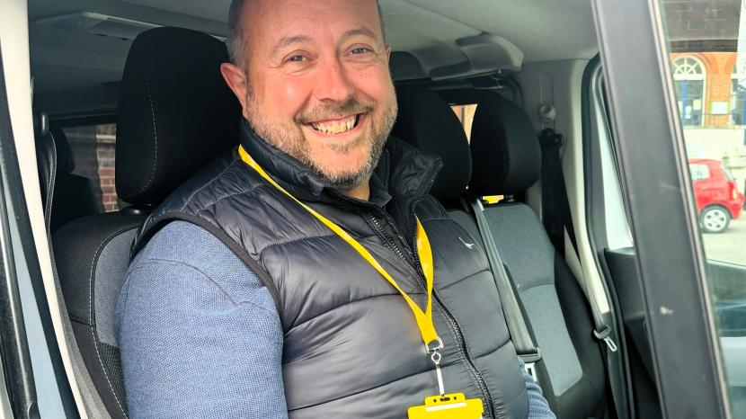 Graham sits in a van, smiling. He is wearing a yellow lanyard.