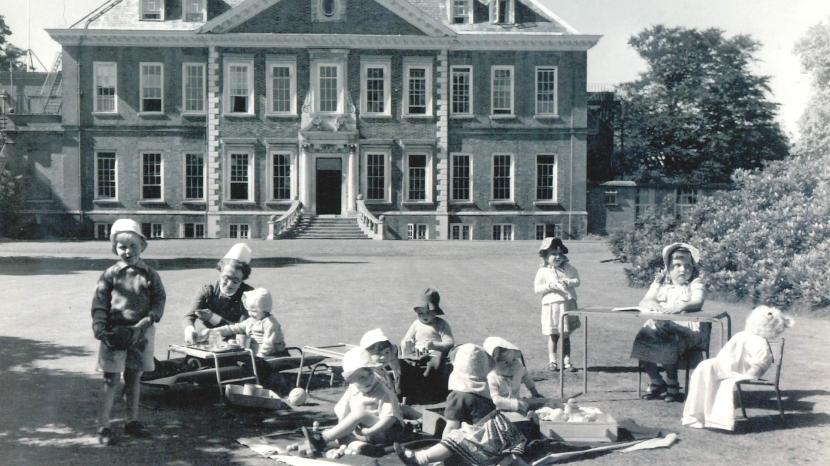 children sitting in the gardens in front of the mansion.